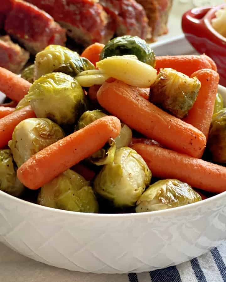 White bowl filled with roasted baby carrots and brussels sprouts.