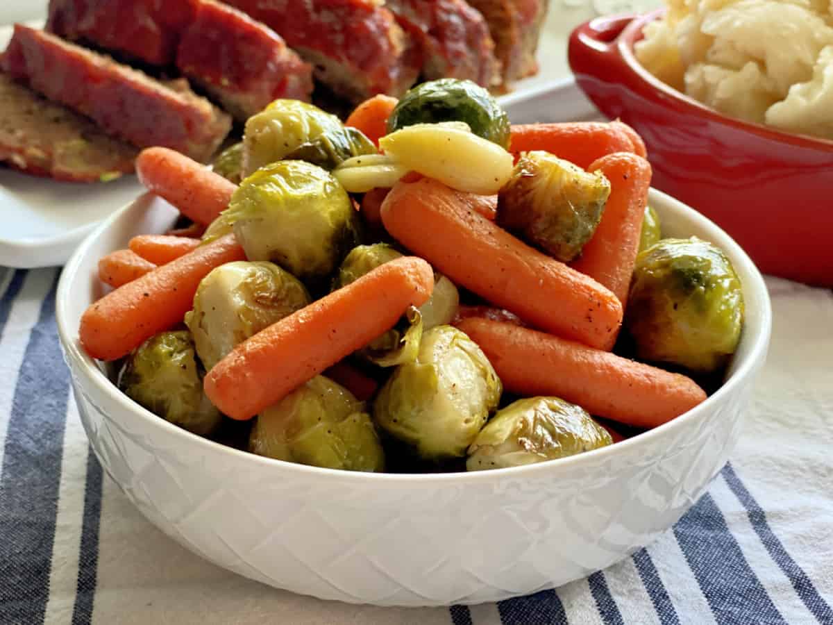 White bowl filled with roasted baby carrots and brussels sprouts.