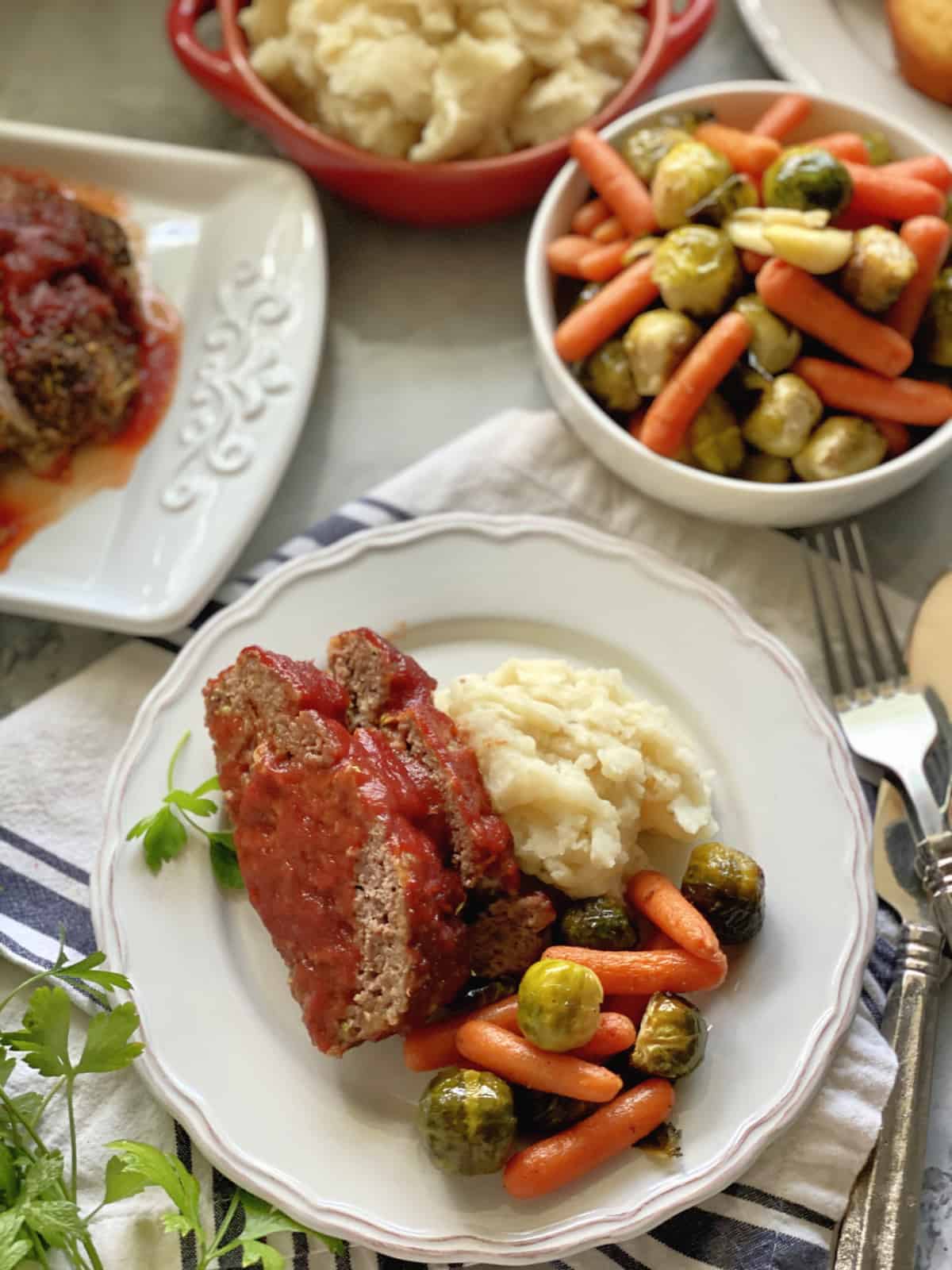 Top view of a plate of meatloaf, mashed potatoes, and veggies, with sides around it.