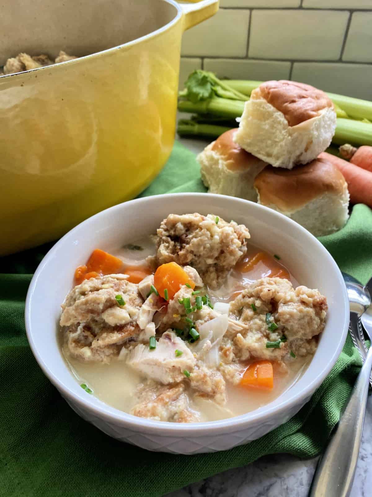 One white bowl filled with Turkey and Stuffing Dumpling Soup with a yellow pot in the background.