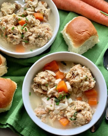 Top view of two bowls of Turkey and Stuffing Dumpling Soup with dinner rolls on the side.