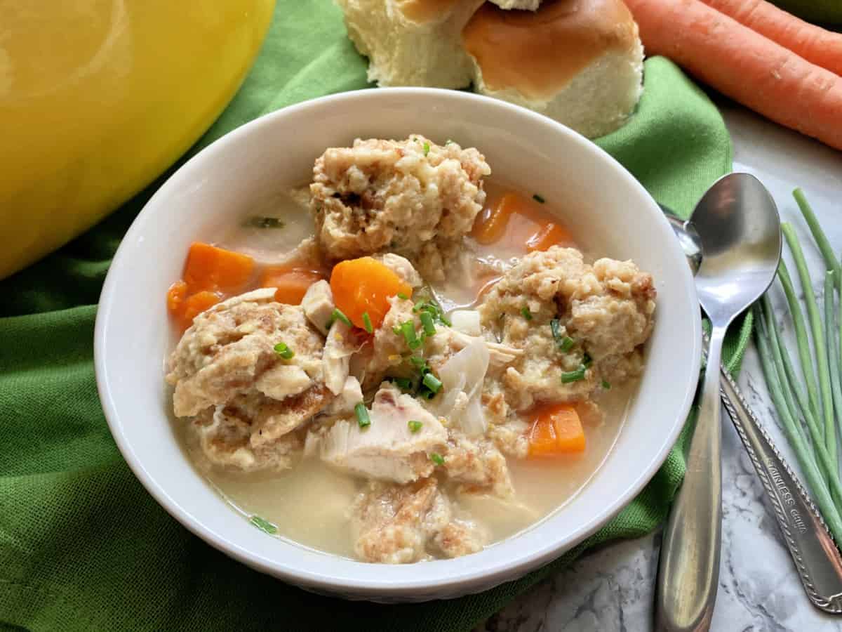 One white bowl filled with Turkey and Stuffing Dumpling soup with spoon on the side.