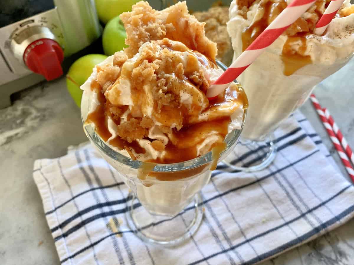 Close up of a Apple Pie Milkshake topped with whipped cream adn caramel sauce.