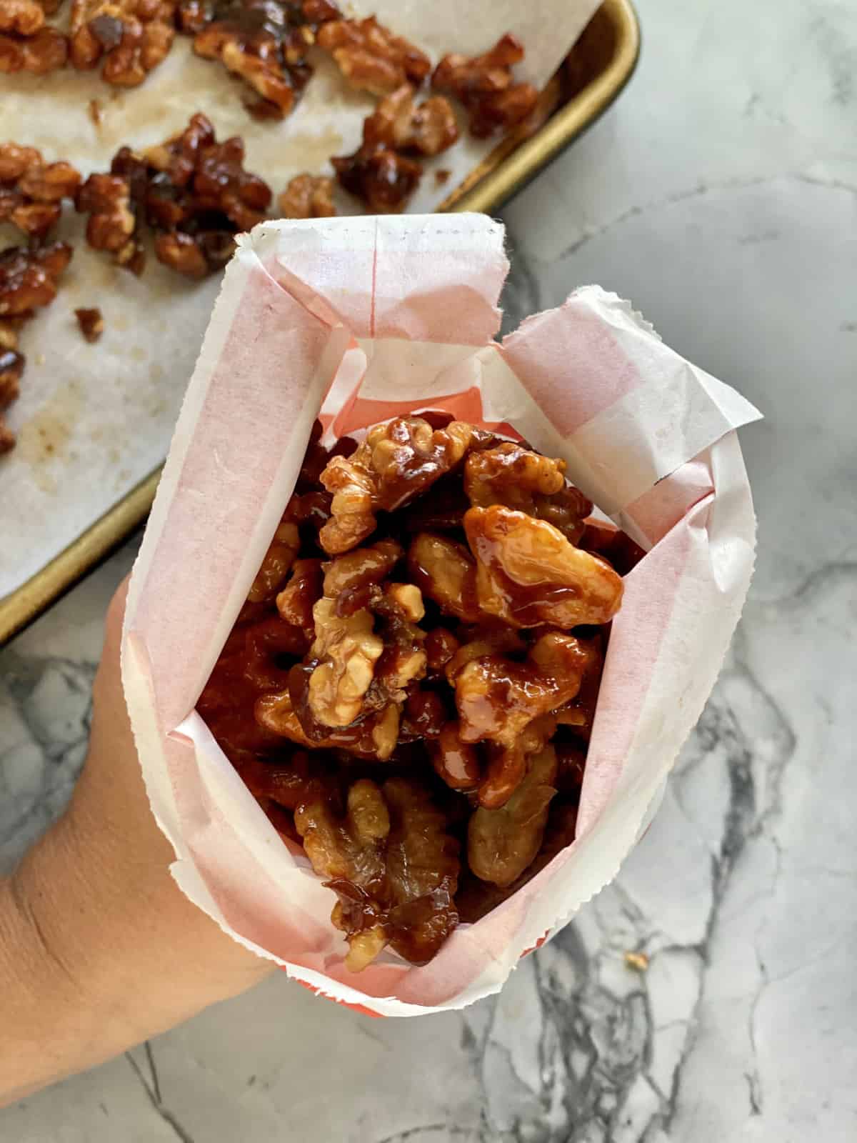 Top view of a hand holding a bag of Candied Walnuts.