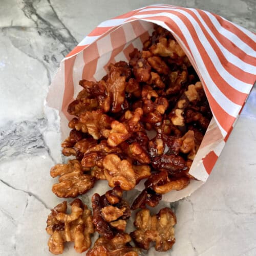 Orange and white striped bag filled with candied walnuts laying on a marble counter.