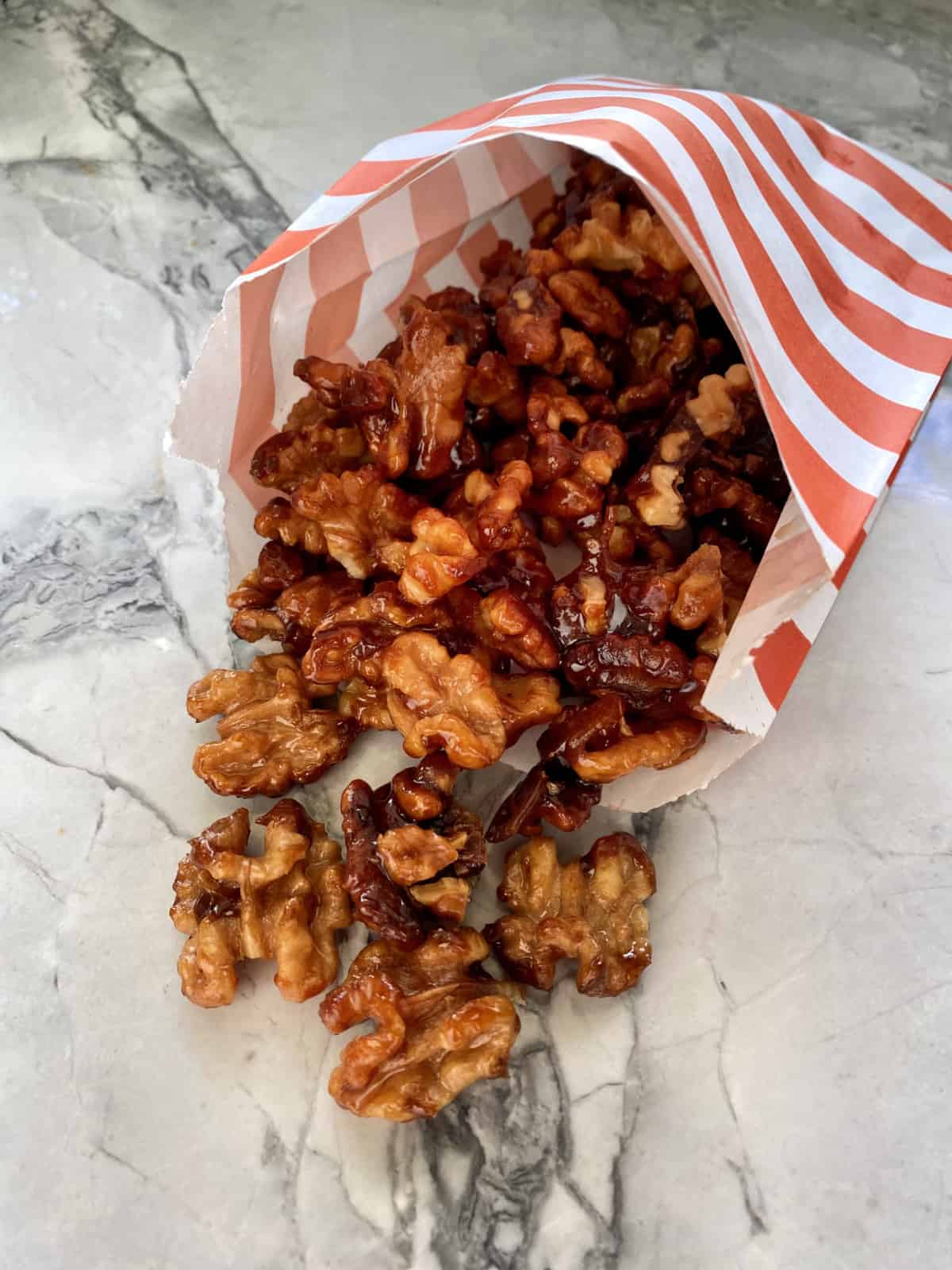 White and orange paper bag filled with candied walnuts.