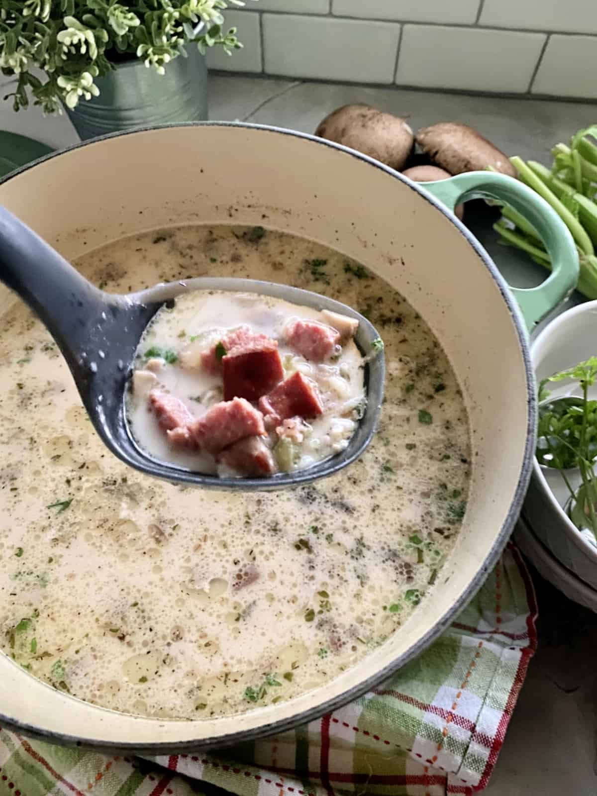 Black ladle holding up a scoop of sausage and wild rice soup over green pot.