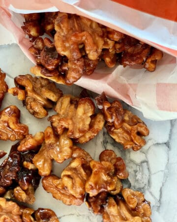 Close up of candied walnuts spilling out of an orange and white bag.