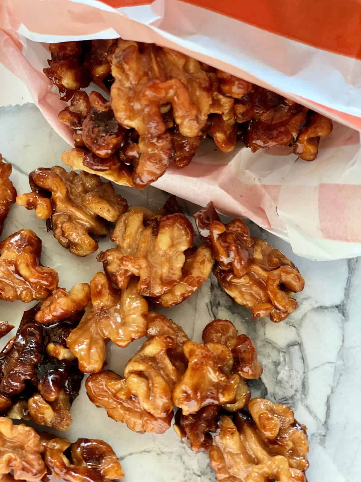 Close up of candied walnuts spilling out of an orange and white bag.