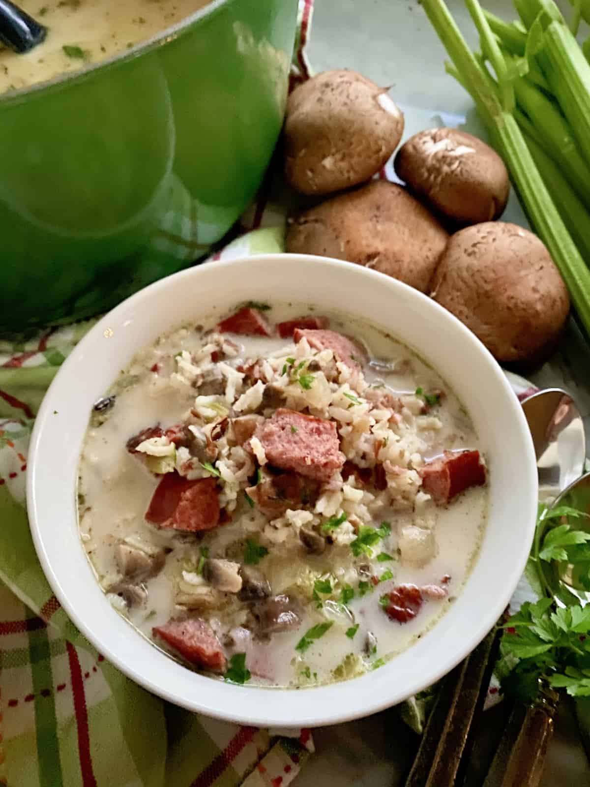 Bowl filled with sausage and wild rice soup with soup pot in background.