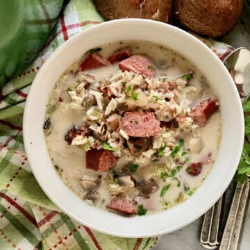 Top view of a white bowl filled with sausage, mushroom, parsley, and rice soup.