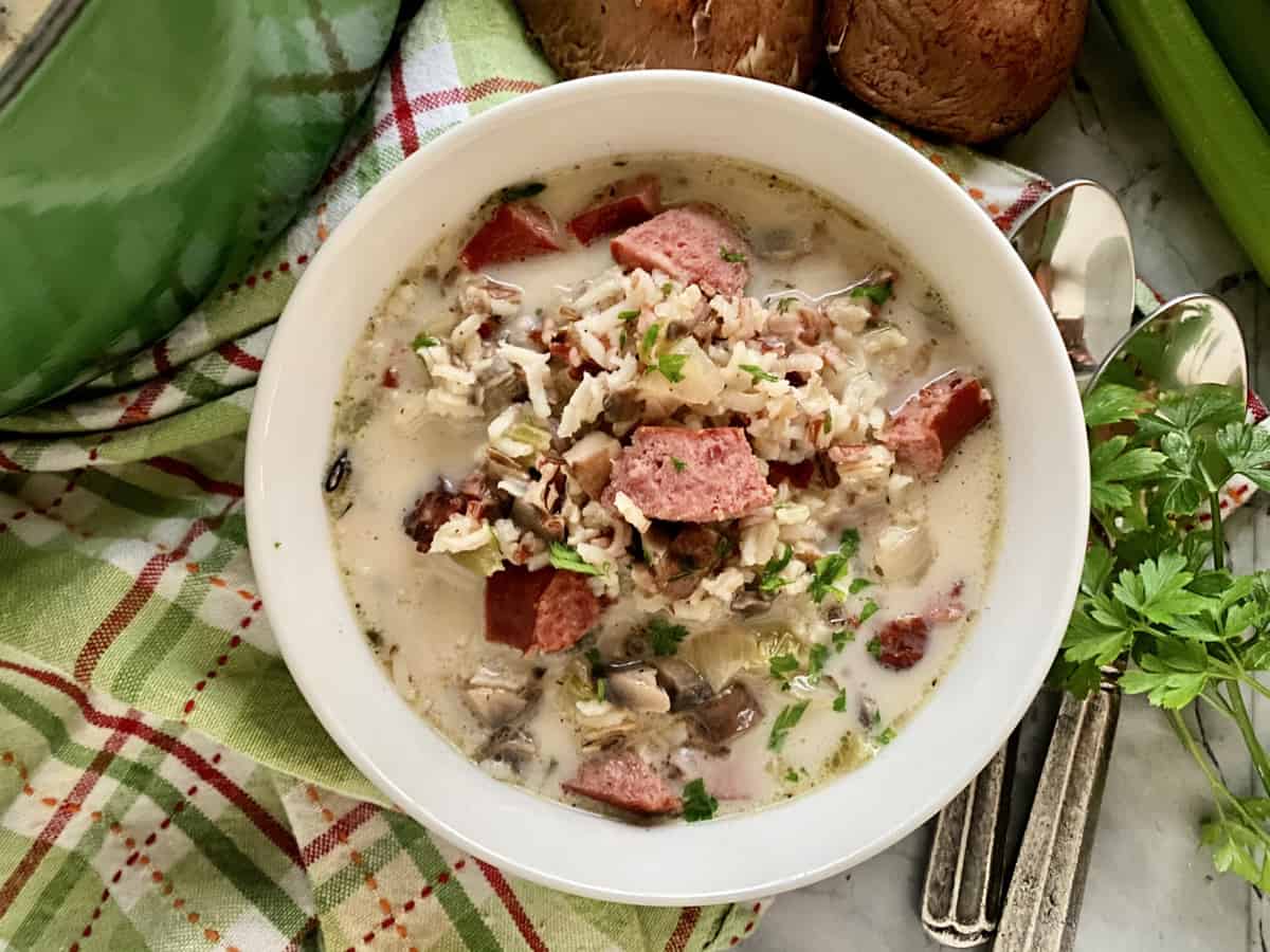 Top view of a white bowl filled with sausage, mushroom, parsley, and rice soup.