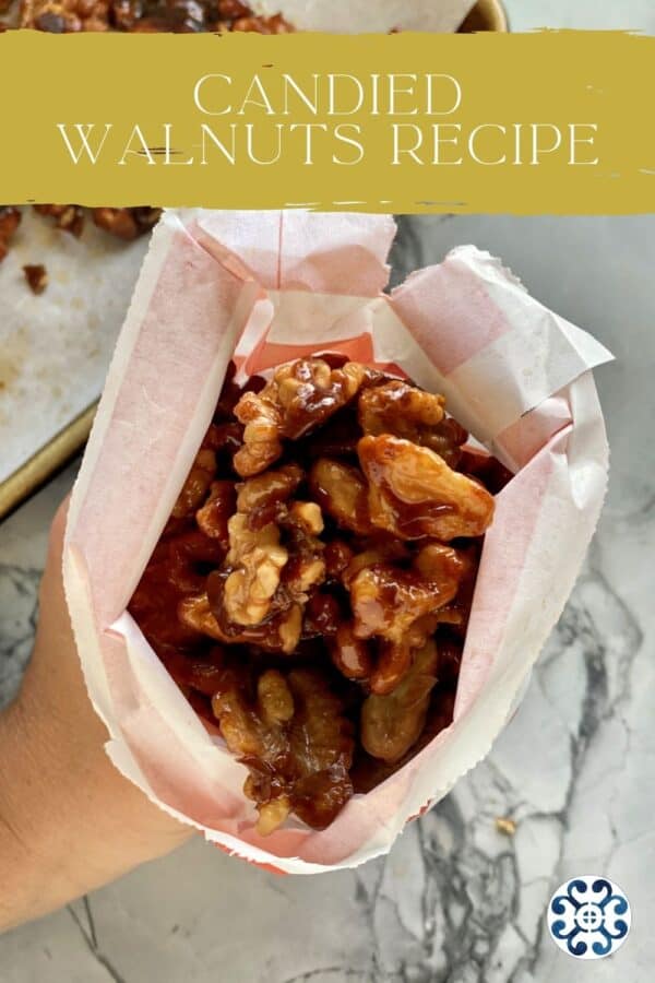Top view of a hand holding a paper bag of candied walnuts with text on image for Pinterest.