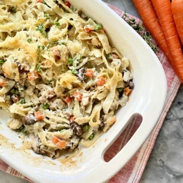 White baking dish filled with pasta, cheese, turkey, carrots, and peas.