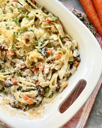 White baking dish filled with pasta, cheese, turkey, carrots, and peas.