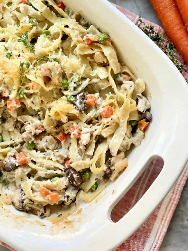 White baking dish filled with pasta, cheese, turkey, carrots, and peas.