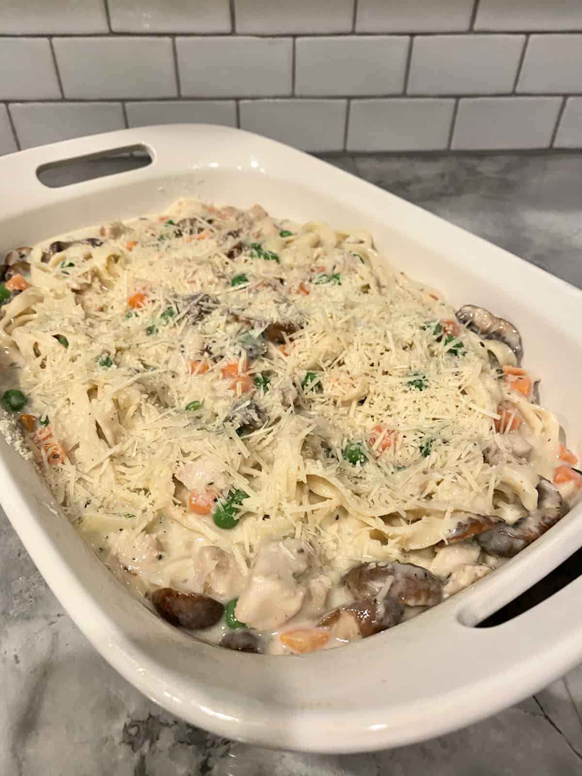 A casserole dish filled with creamy pasta, mushrooms, and turkey topped with cheese.