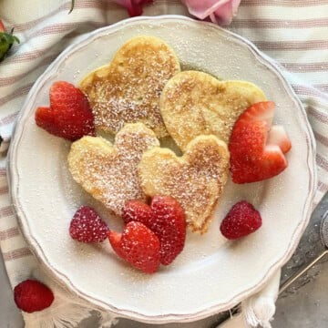 white plate with heart shaped pancakes and strawberries.