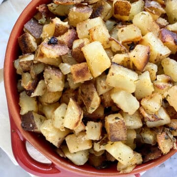 Top view of a red bowl filled with diced crispy breakfast potatoes.