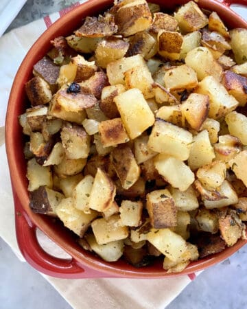 Top view of a red bowl filled with diced crispy breakfast potatoes.