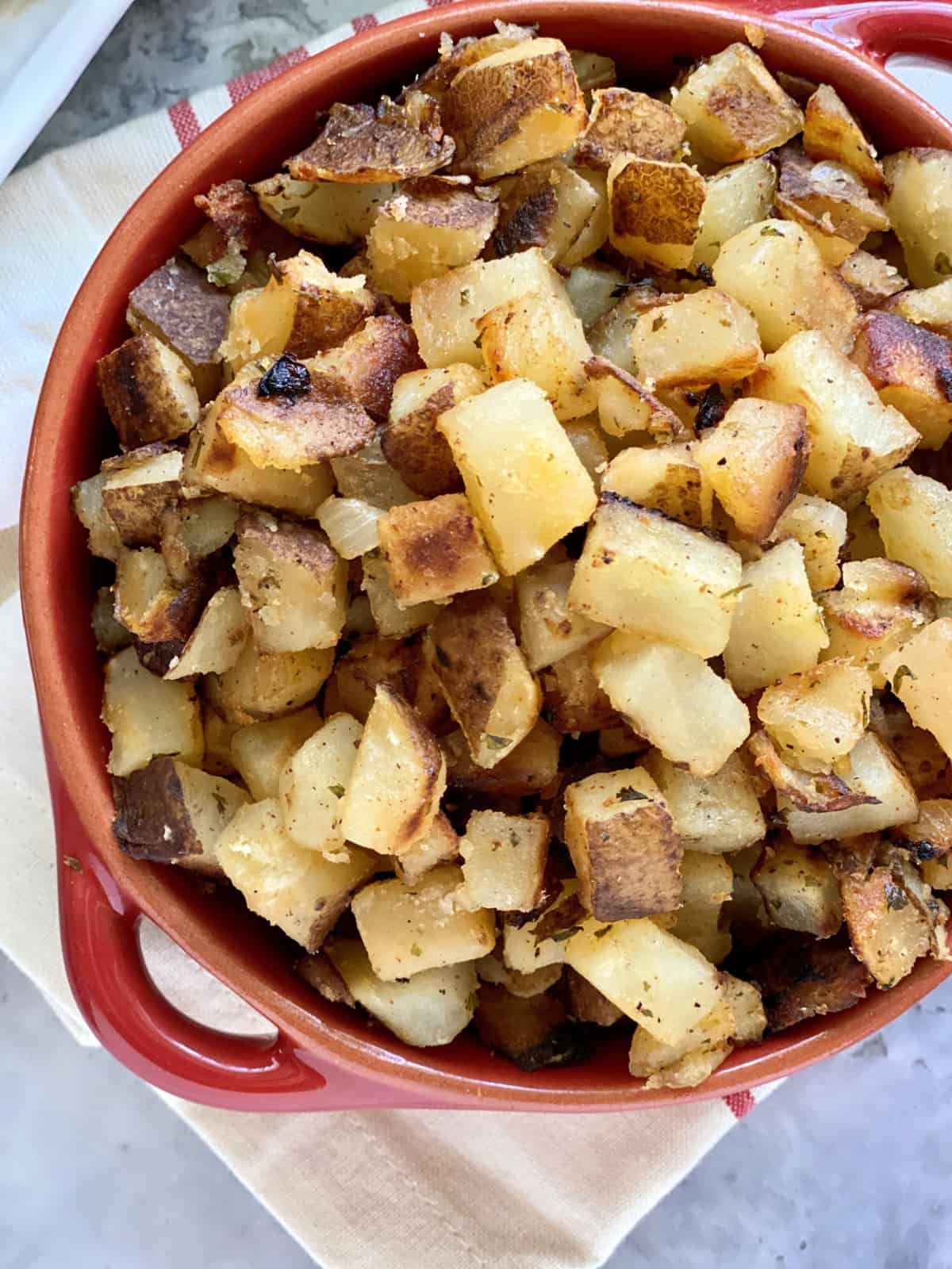 Top view of a red bowl filled with diced crispy breakfast potatoes.