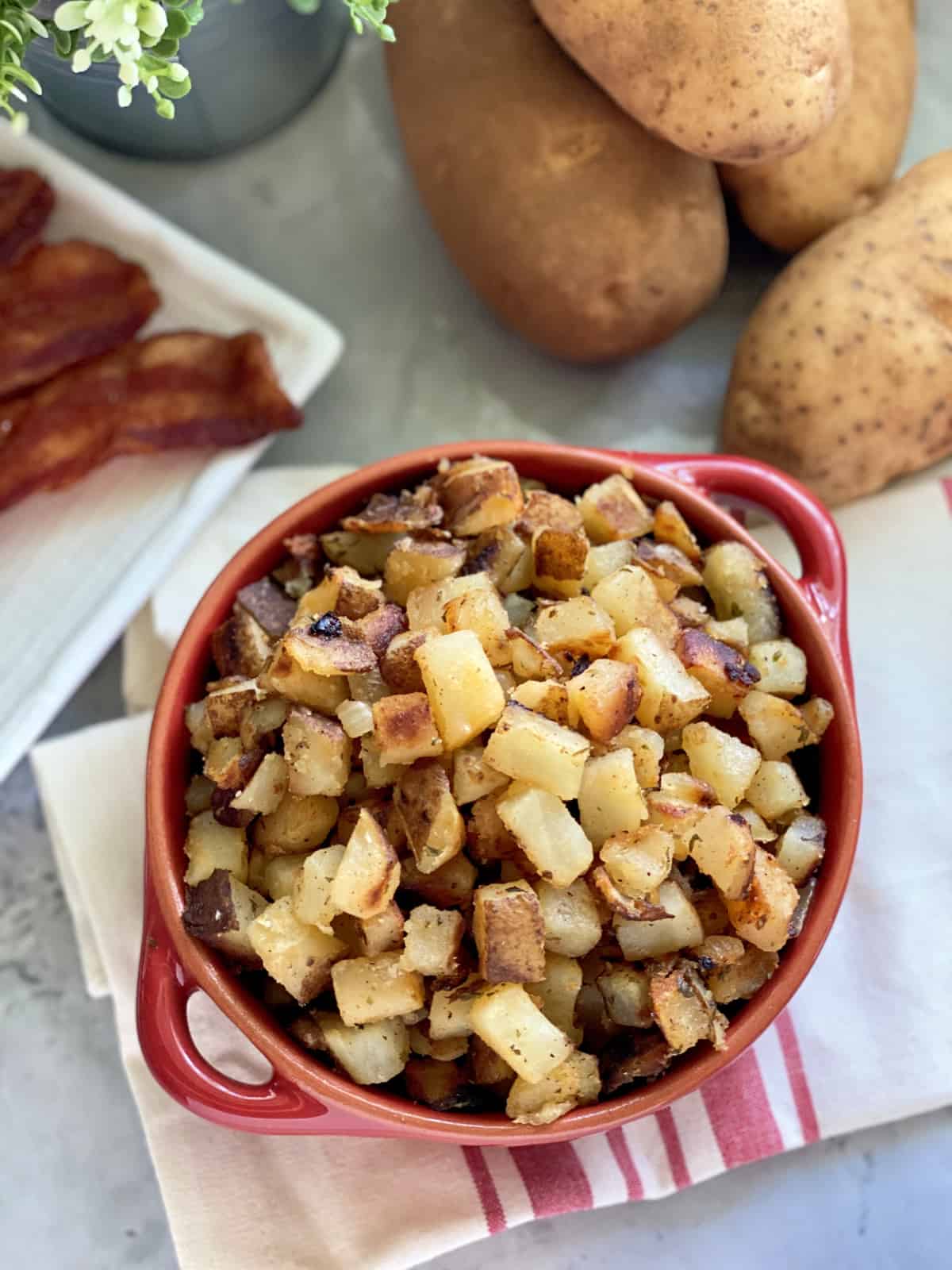 Top view of a red bowl filled with diced potatoes on a red and white striped cloth.