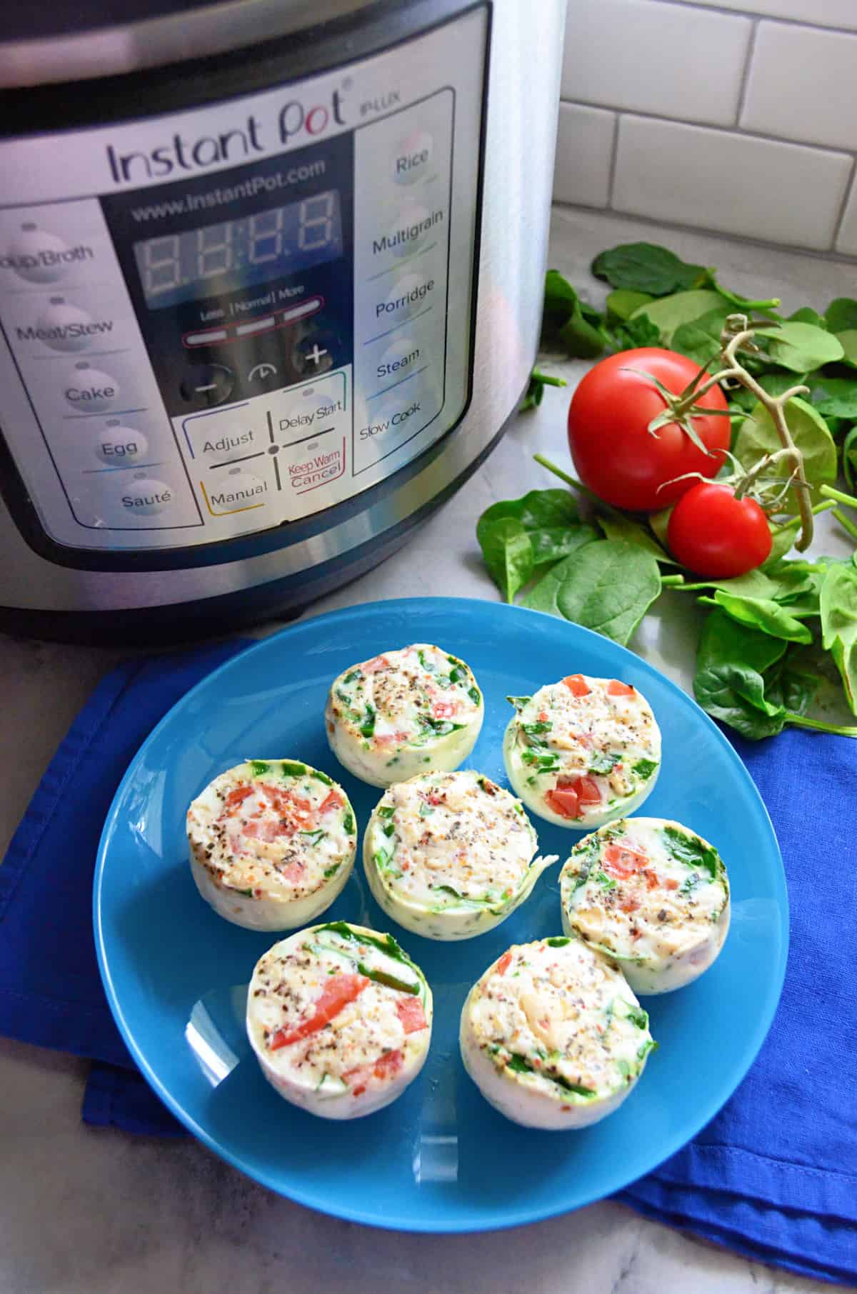 Top view of 7 egg bites on a blue plate with Instant Pot and fresh vegetables in background.