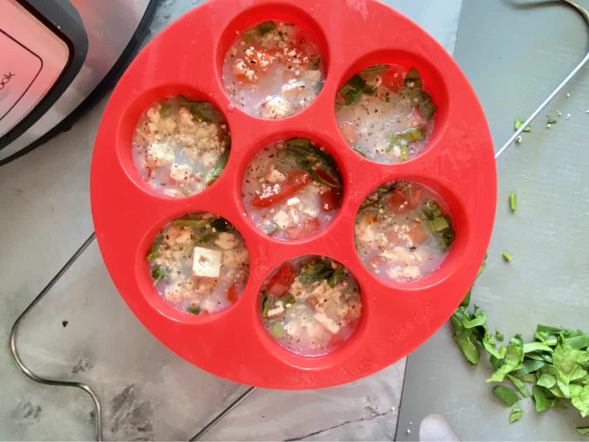 Top view of a silicone mould filled with liquid egg whites, tomatoes, and spinach.