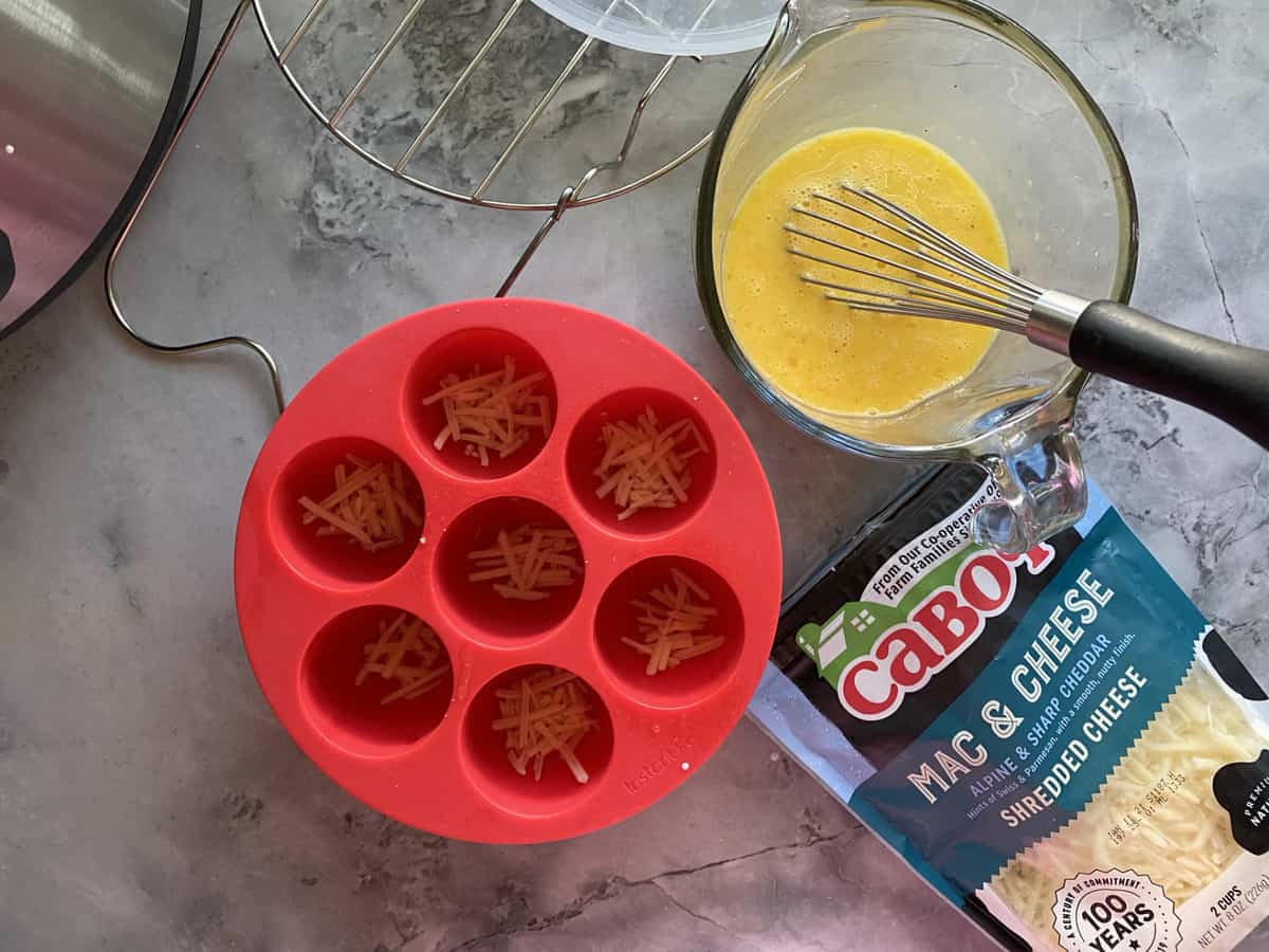 Cheese in the bottom of egg molds with scrambled egg in a glass measuring cup.