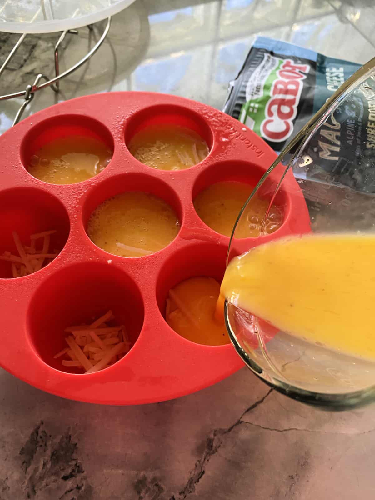 Glass measuring cup pouring eggs into a mold.