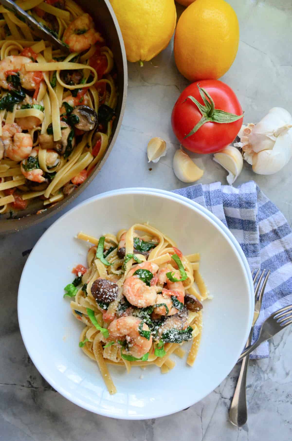 Top view of a white bowl of shrimp pasta with skillet next to it.