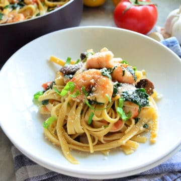 Two shallow white bowls with linguini and shrimp topped with basil ribbons.