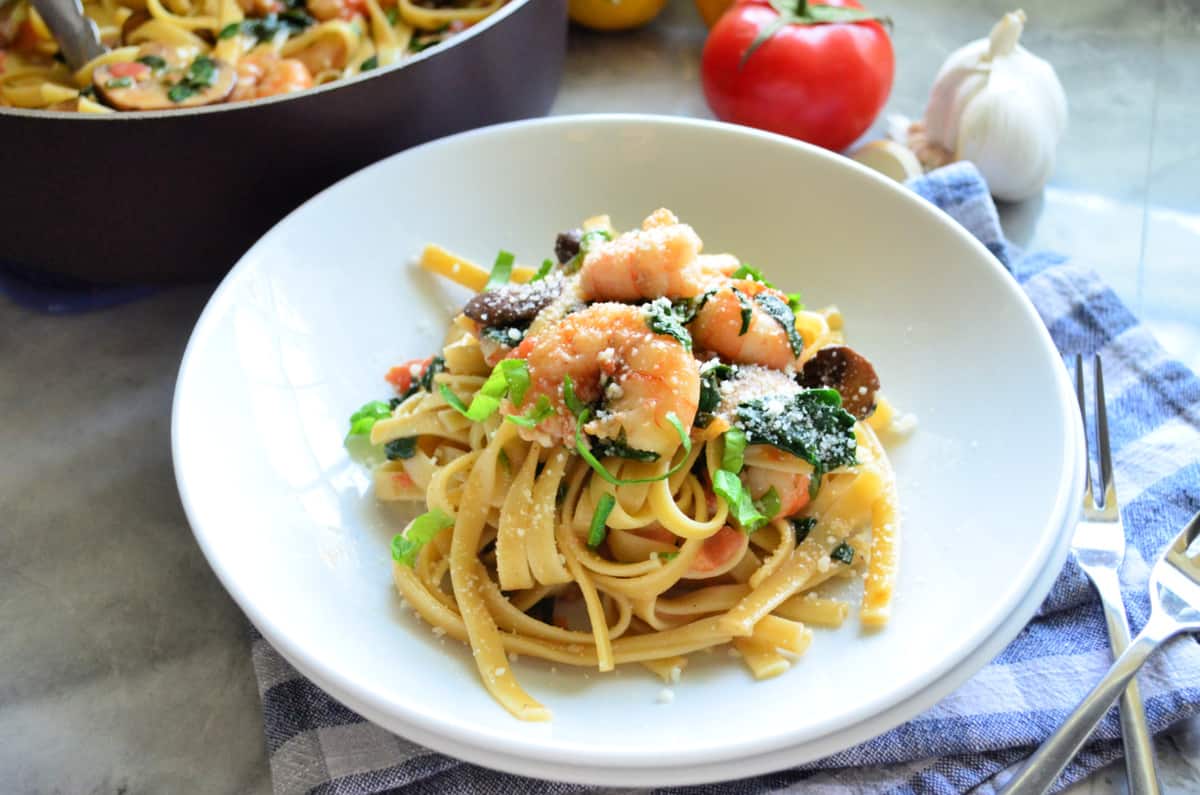 Two shallow white bowls with linguini and shrimp topped with basil ribbons.
