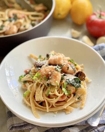 Linguini topped with shrimp nestled in a white bowl.