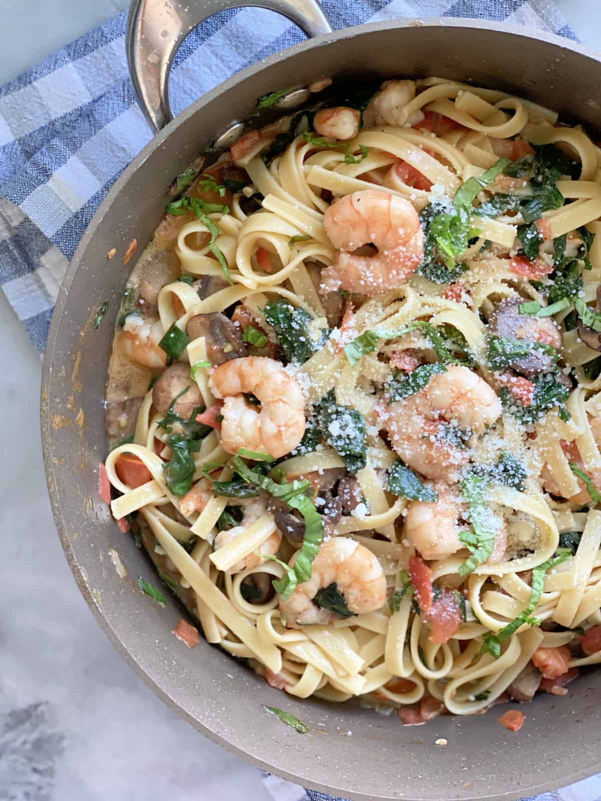 Top view of a pasta with shrimp, spinach, and cheese in a skillet.