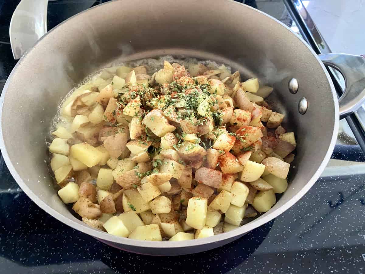 A frying pan cooking diced potatoes with seasoning on top.