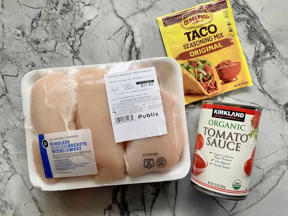 Ingredients on marble counter: chicken breast, taco seasoning, tomato sauce.