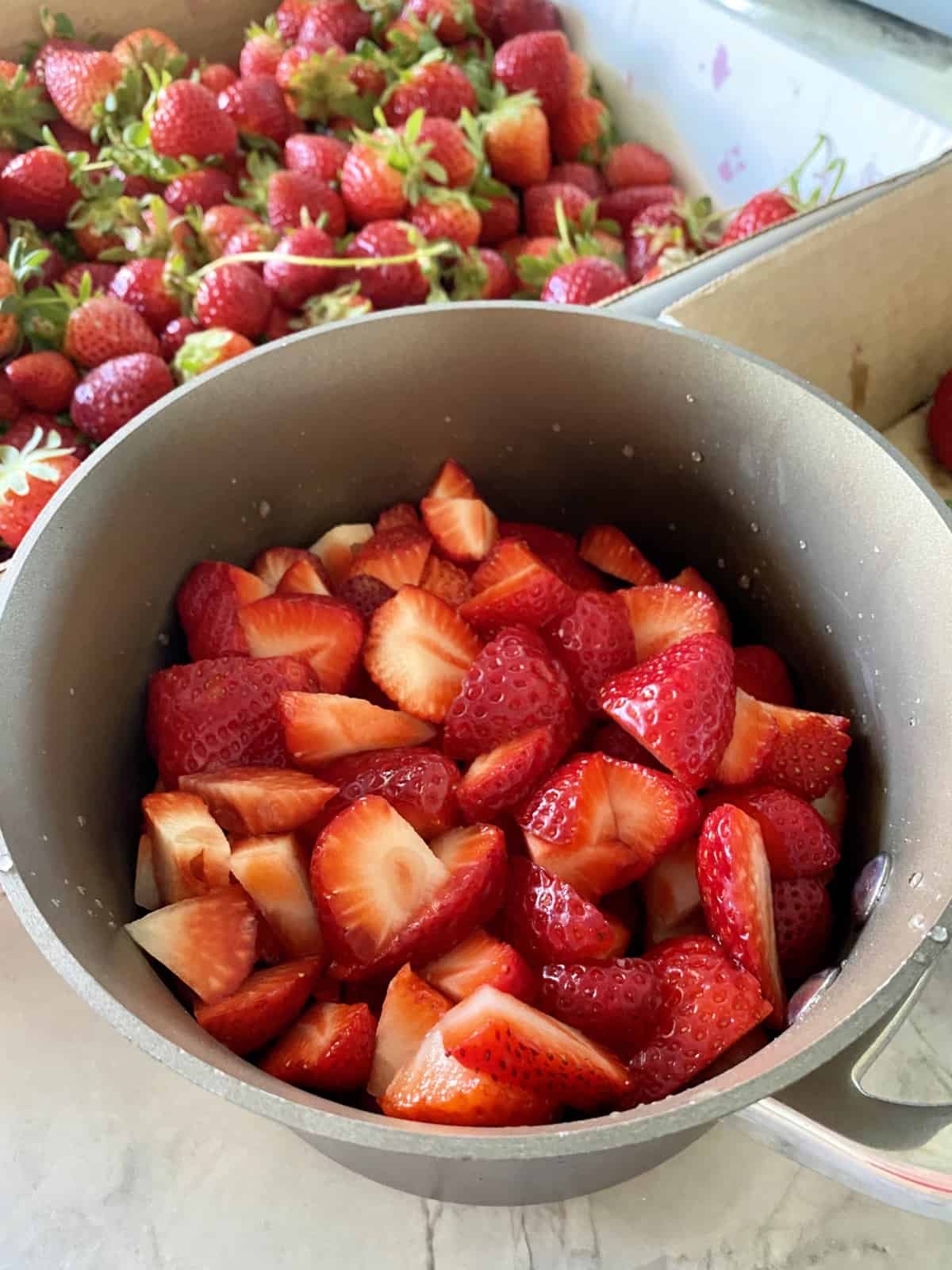 Sauce pot filled with chopped strawberries and strawberries in the background.
