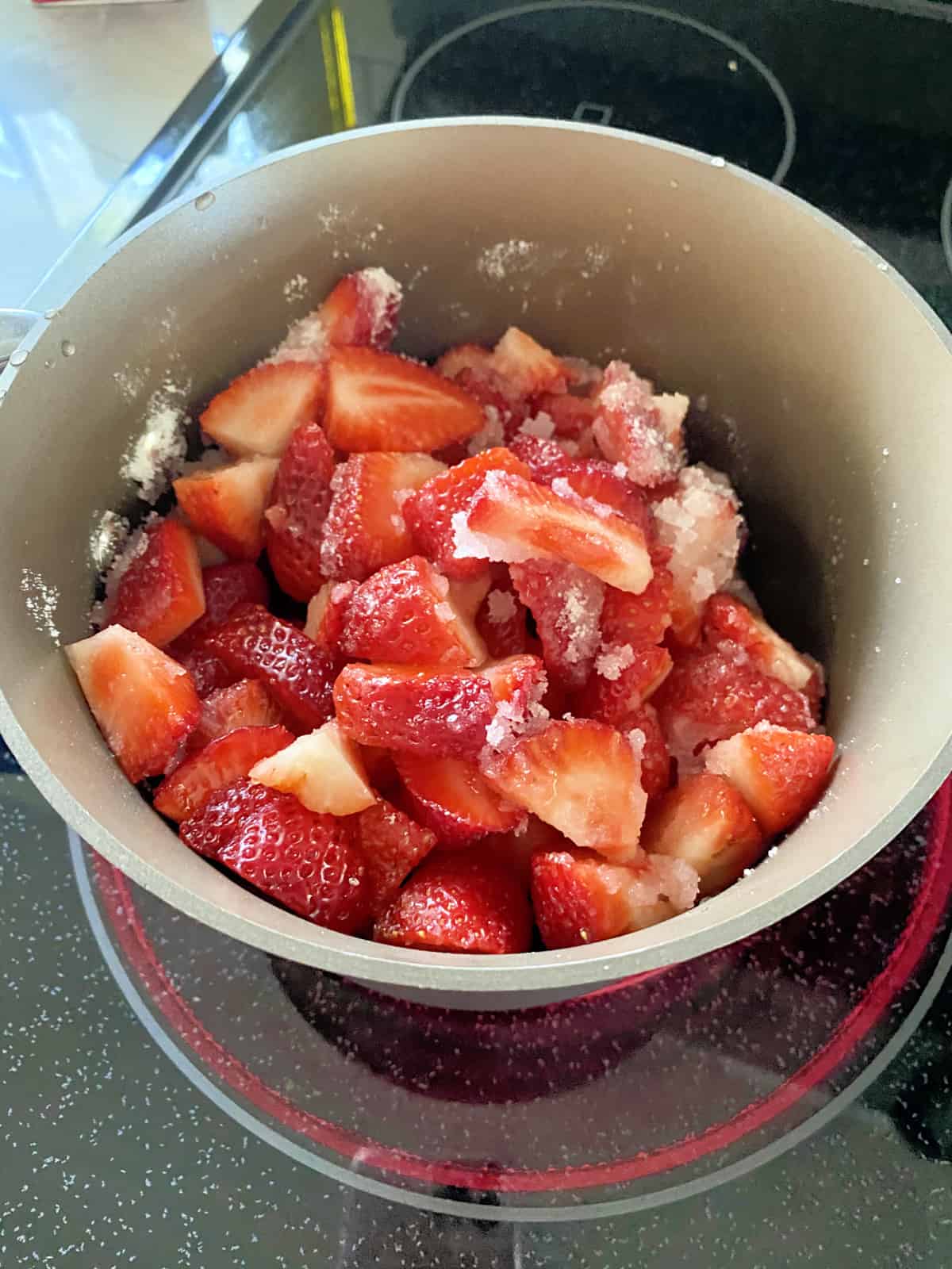 Sauce pot of strawberries mixed with sugar in a sauce pot.