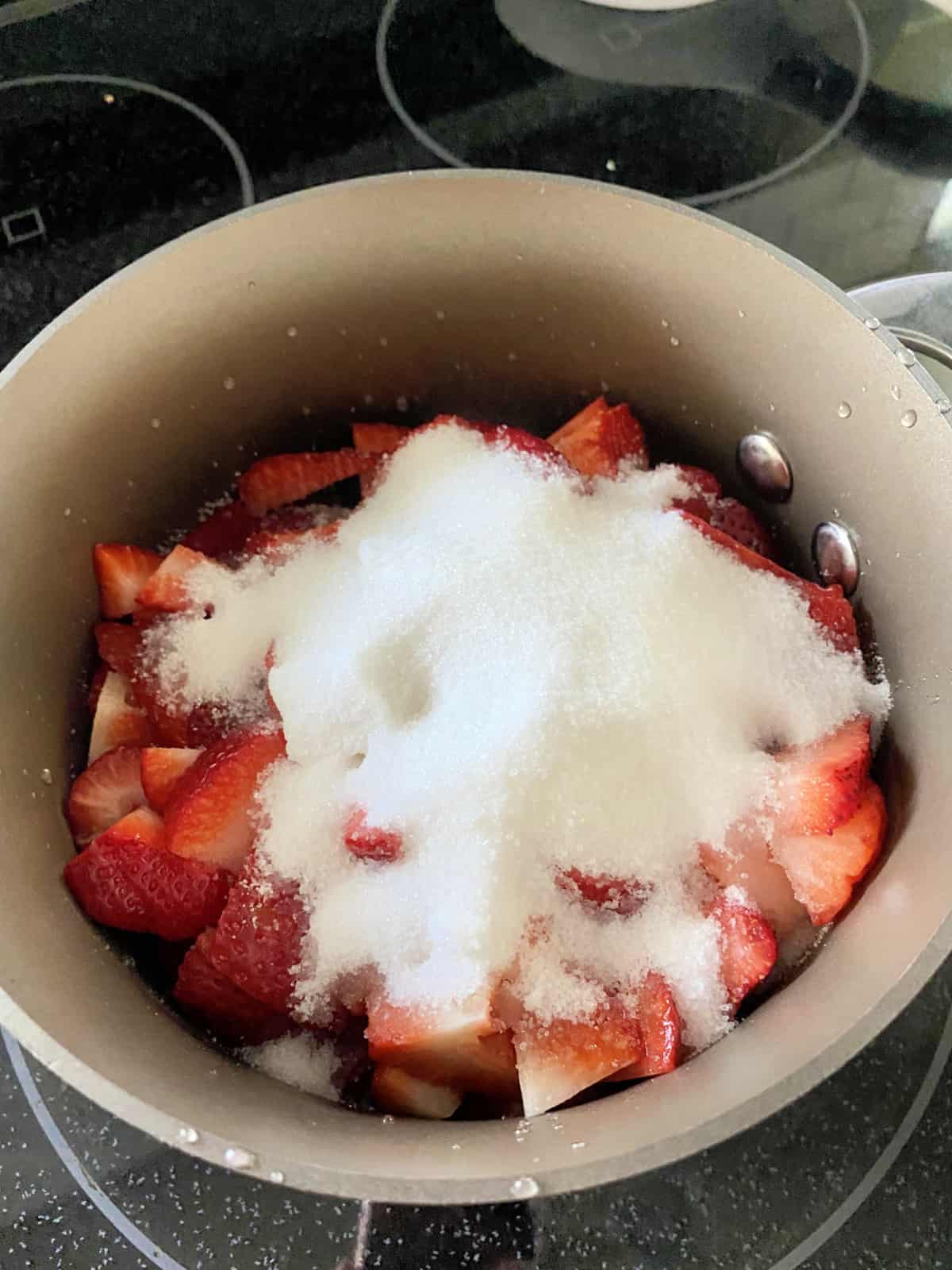 Sauce pot filled with chopped strawberries with granulated white sugar on top.