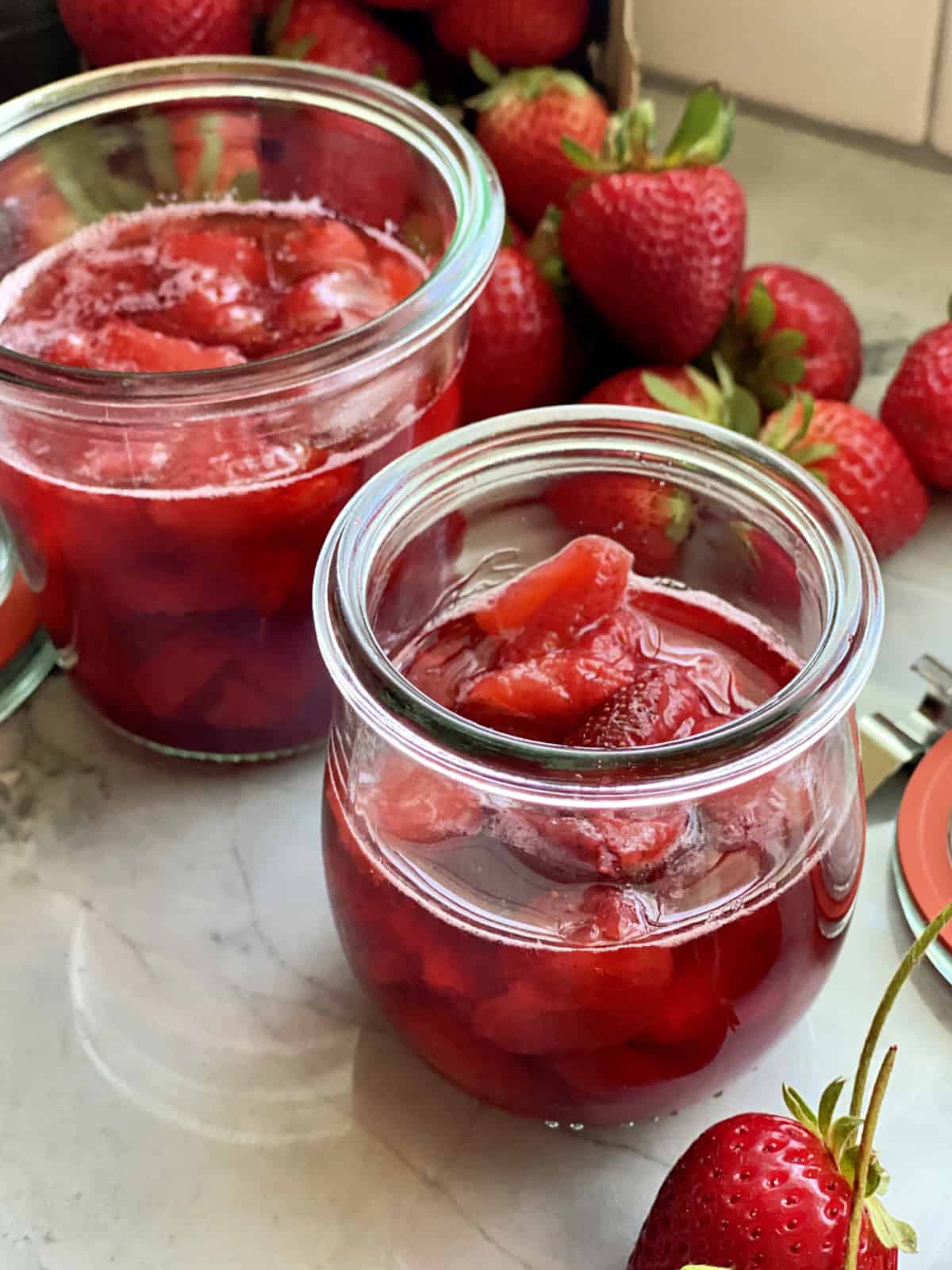 Close up of two glass jars filled with strawberry sauce.