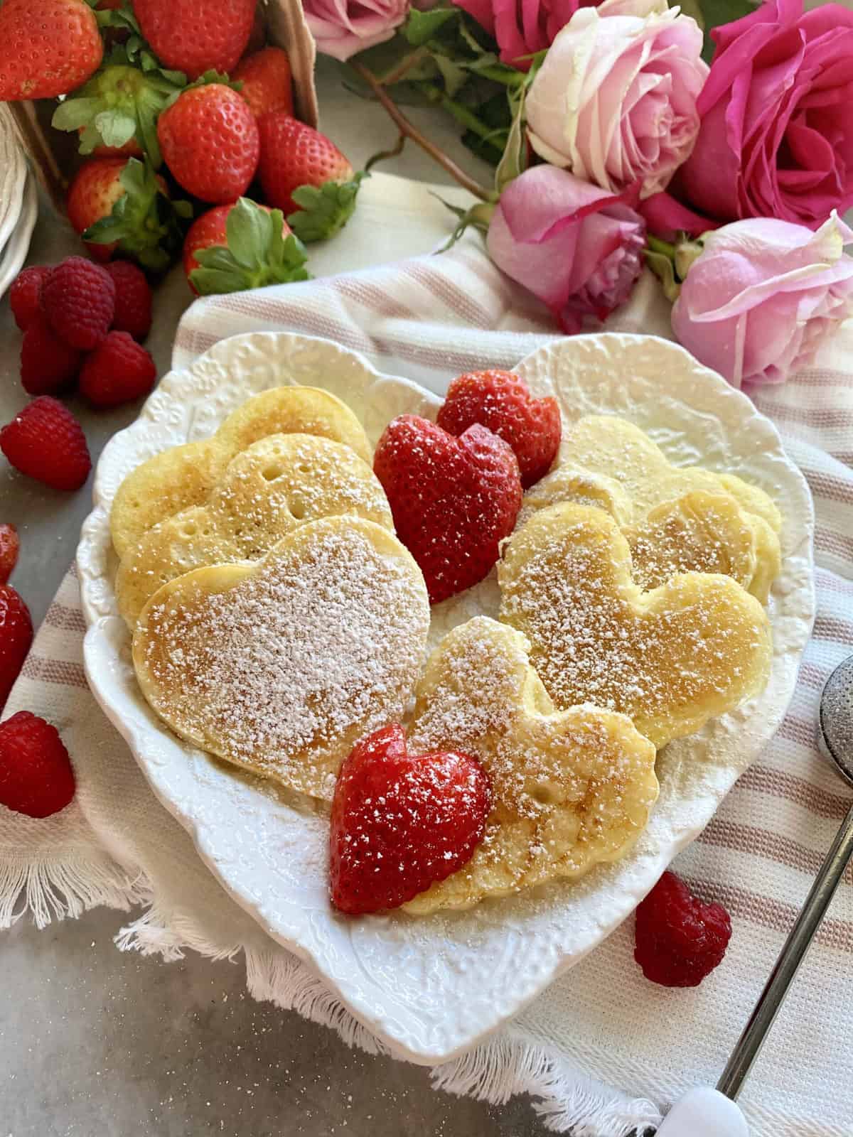 Heart shaped plate filled with heart shaped pancakes dusted with powder sugar.