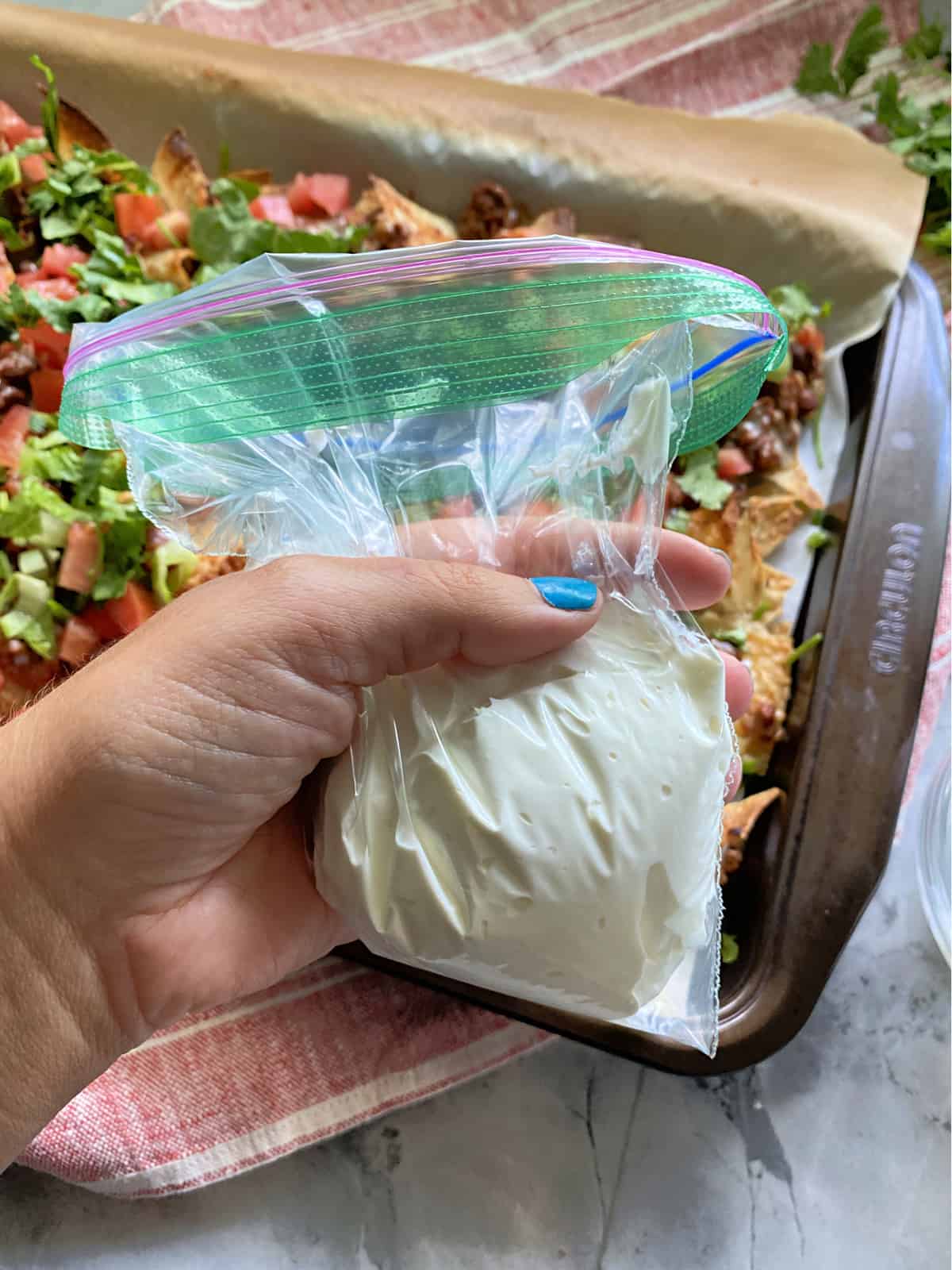 Sour cream in a ziploc baggy with nachos in the background.