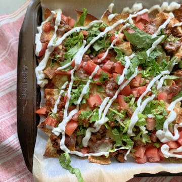 Sheet pan lined with parchment paper with loaded nachos on top.