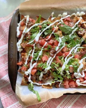 Sheet pan lined with parchment paper with loaded nachos on top.