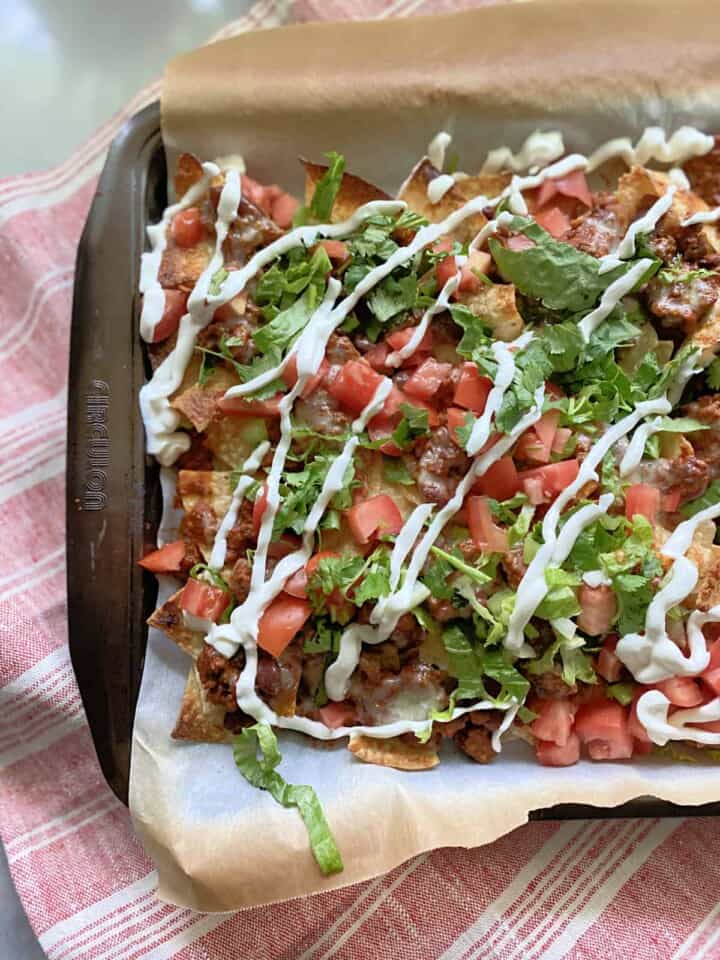 Sheet pan lined with parchment paper with loaded nachos on top.