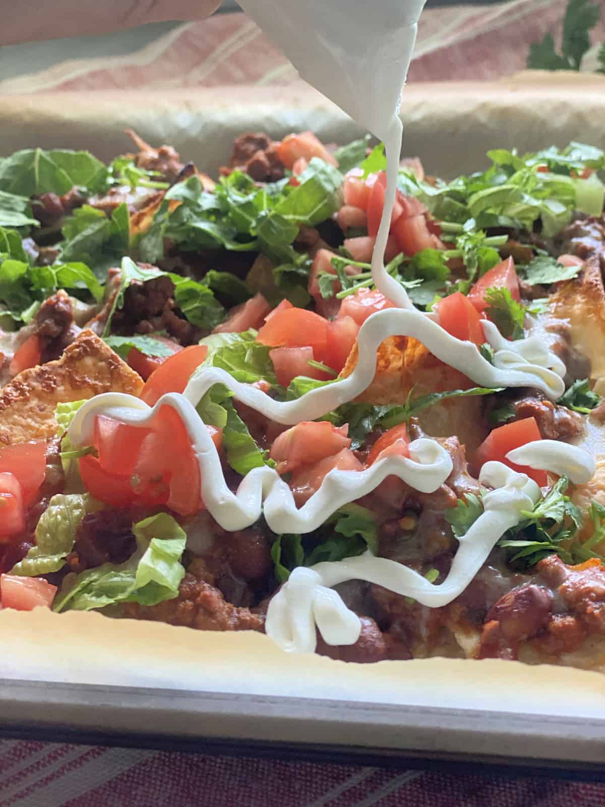 Sour cream drizzling over a sheet pan of nachos.