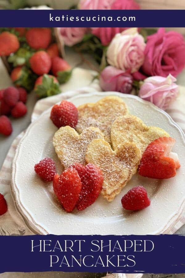 White plate filled with four heart shaped pancakes with heart strawberries with text on image for Pinterest.