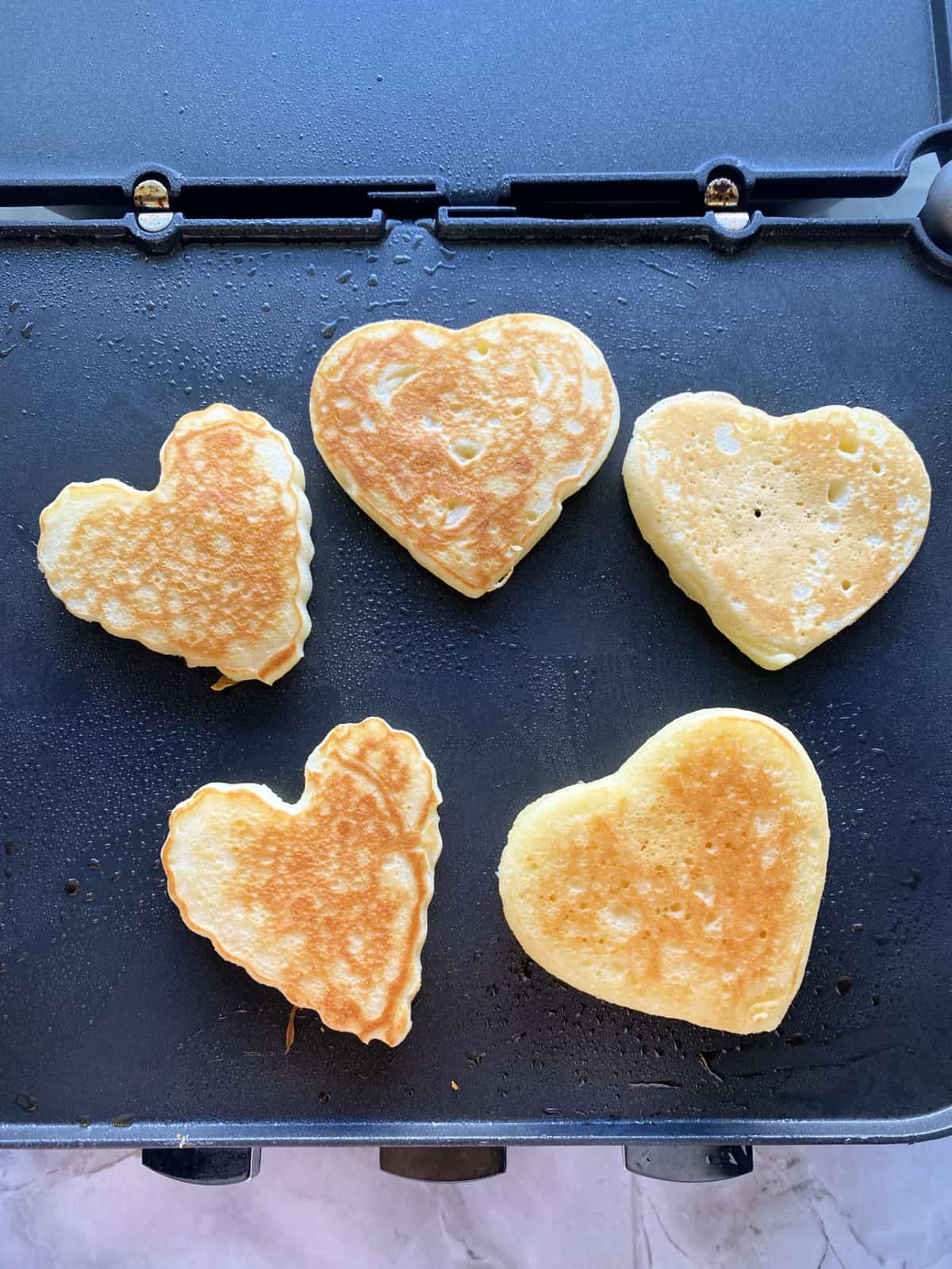 Five heart shaped pancakes on a griddle top. 
