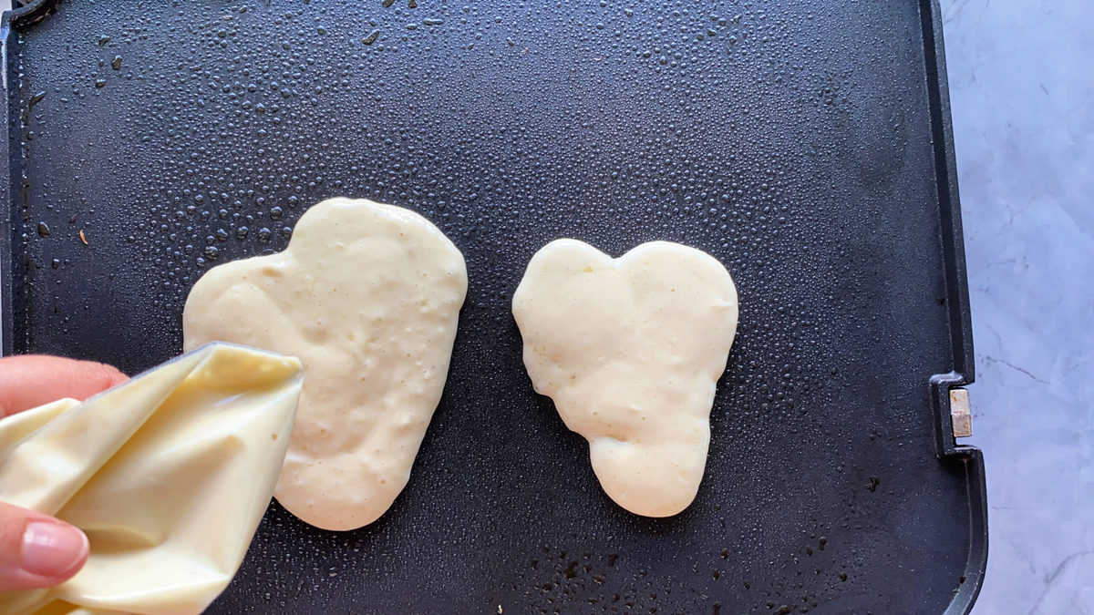 Hand shaping hearts on a griddle using batter in a bag. 